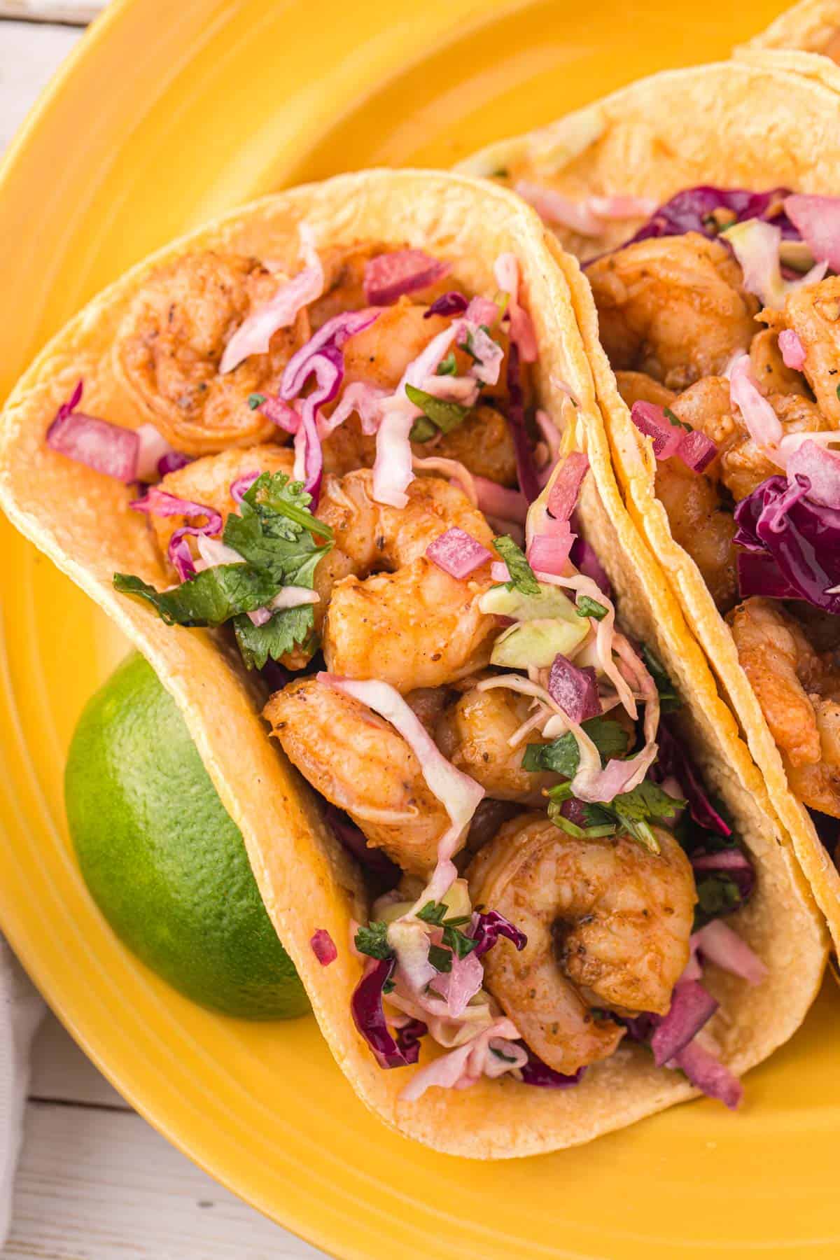 shrimp tacos on a yellow plate with a lime.