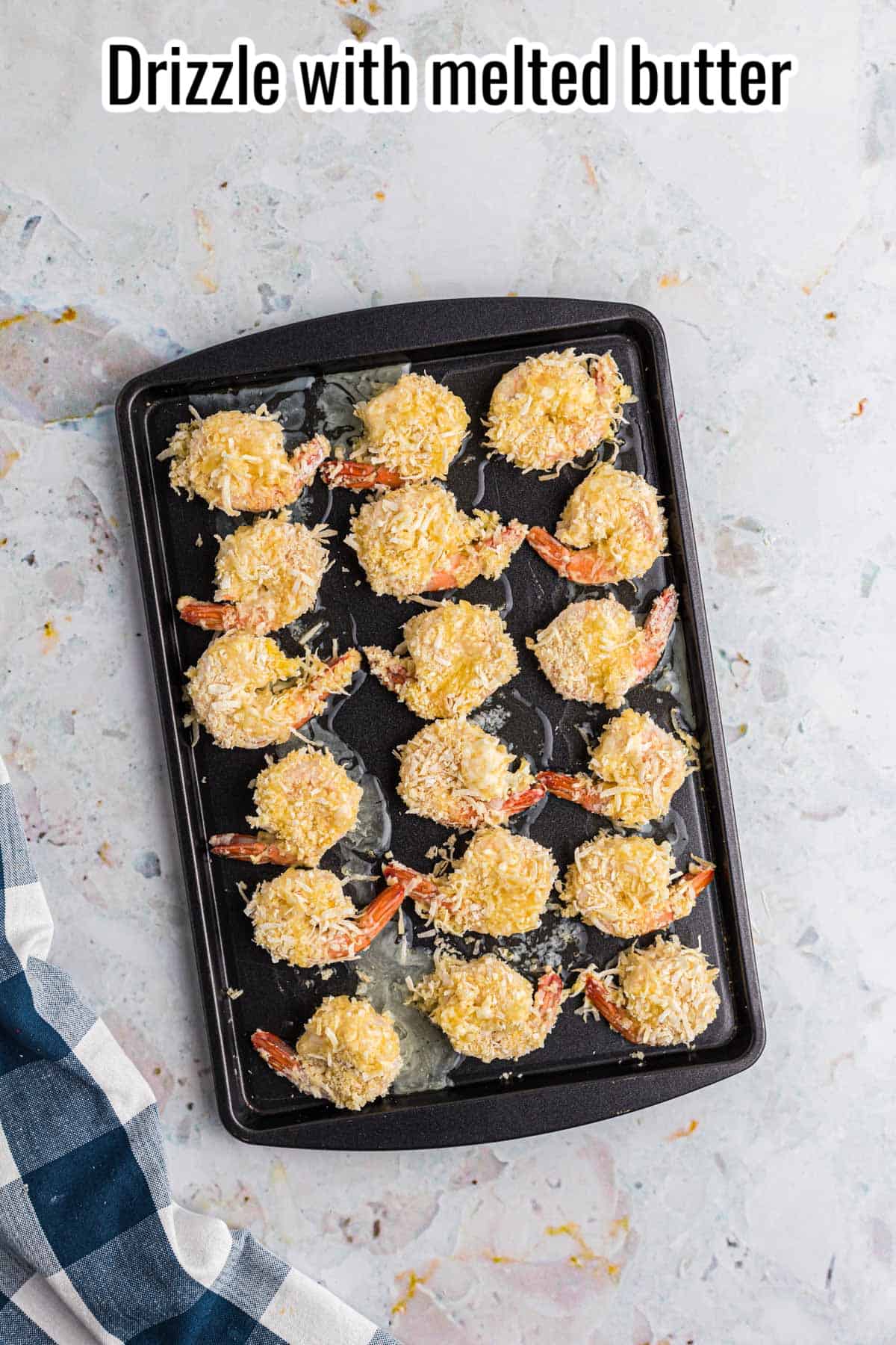 breaded shrimp with butter drizzled over the top on a sheet pan.