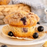 blueberry muffin in a wrapper with blueberries on a plate.