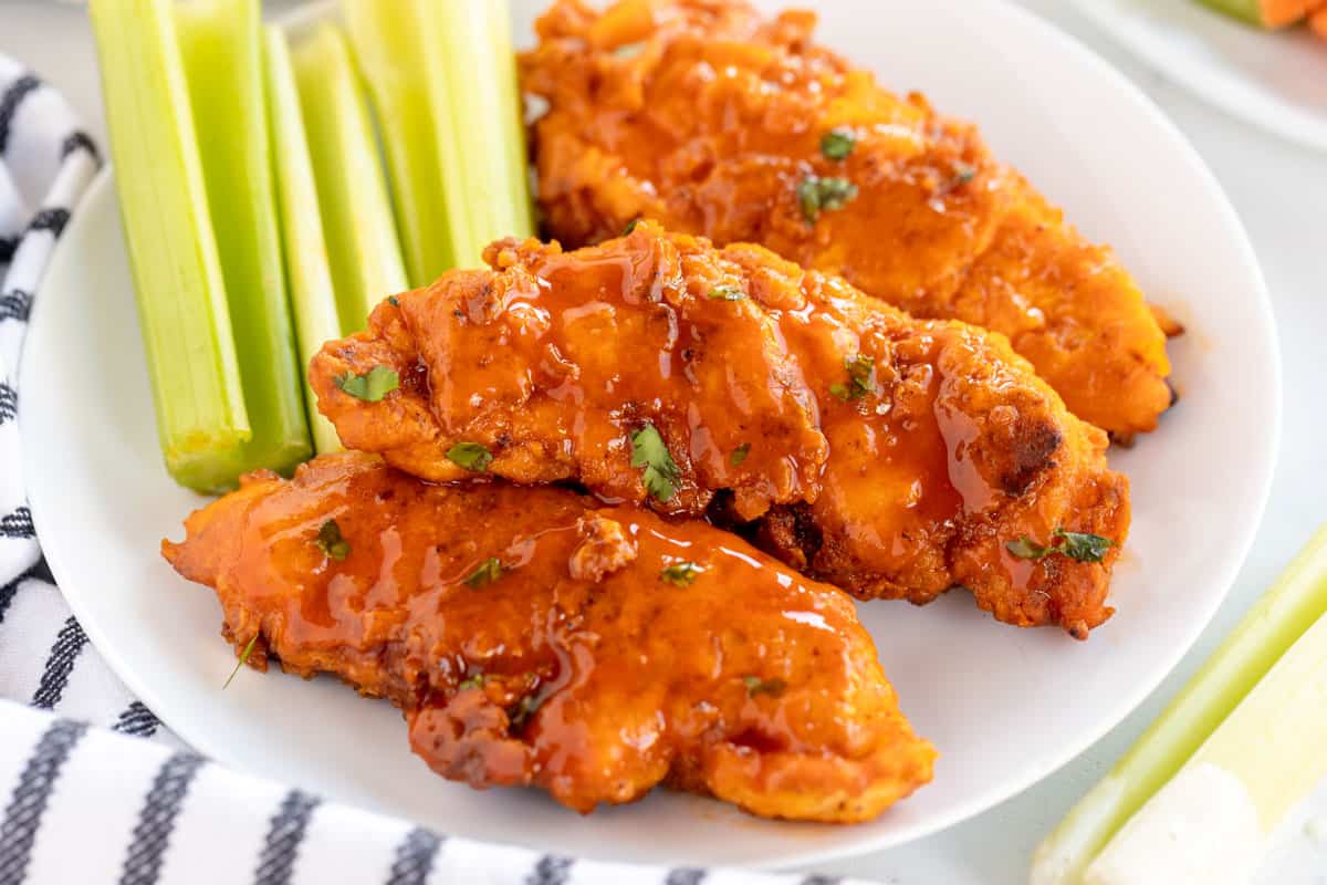 buffalo chicken tenders on a white plate with celery.