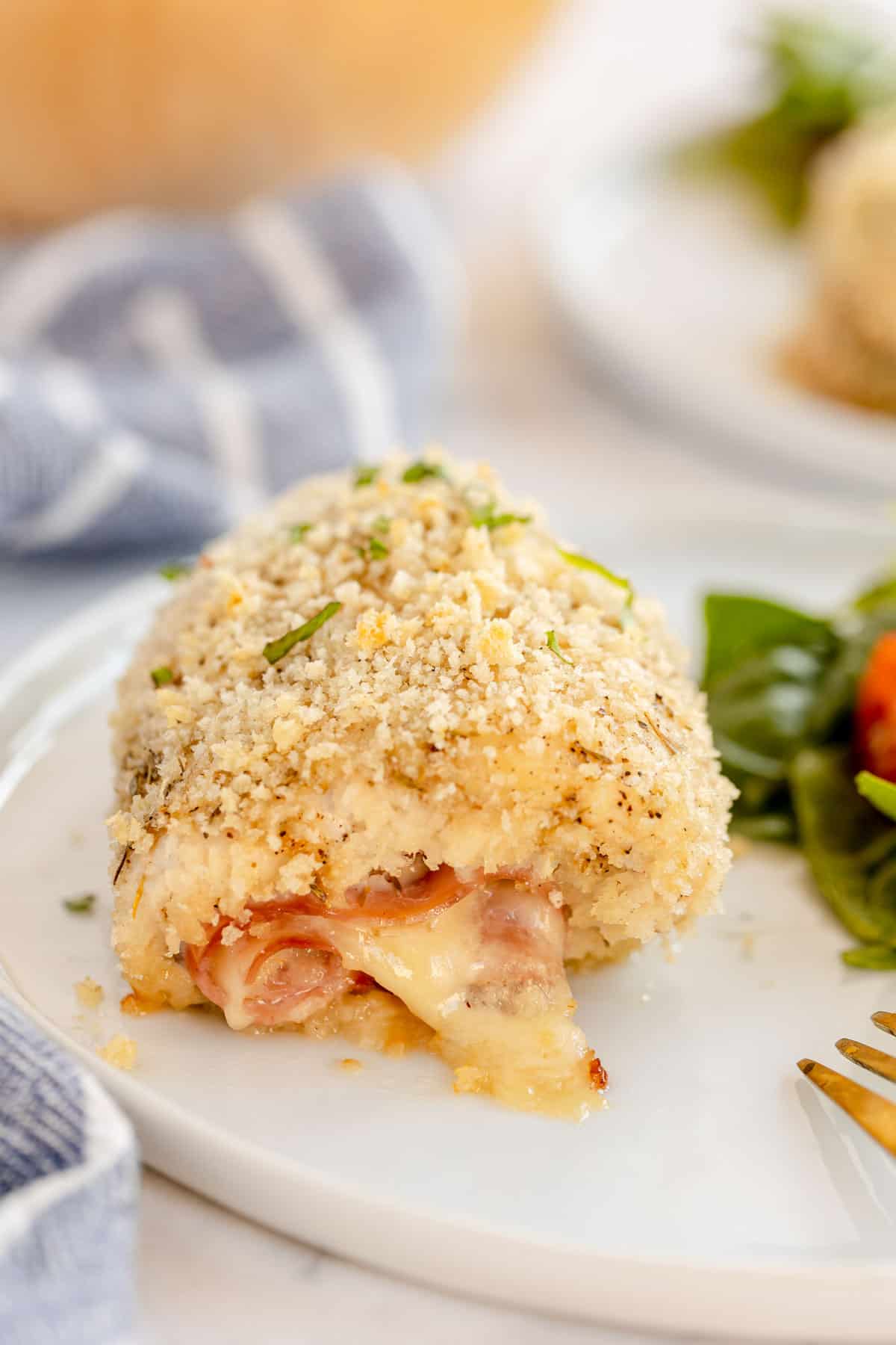 Chicken cordon bleu with salad on a white plate.