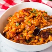 baked beans in a white bowl with red and white napkin.