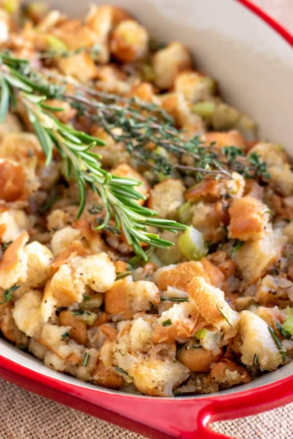 homemade stuffing in a red casserole dish with fresh herbs.