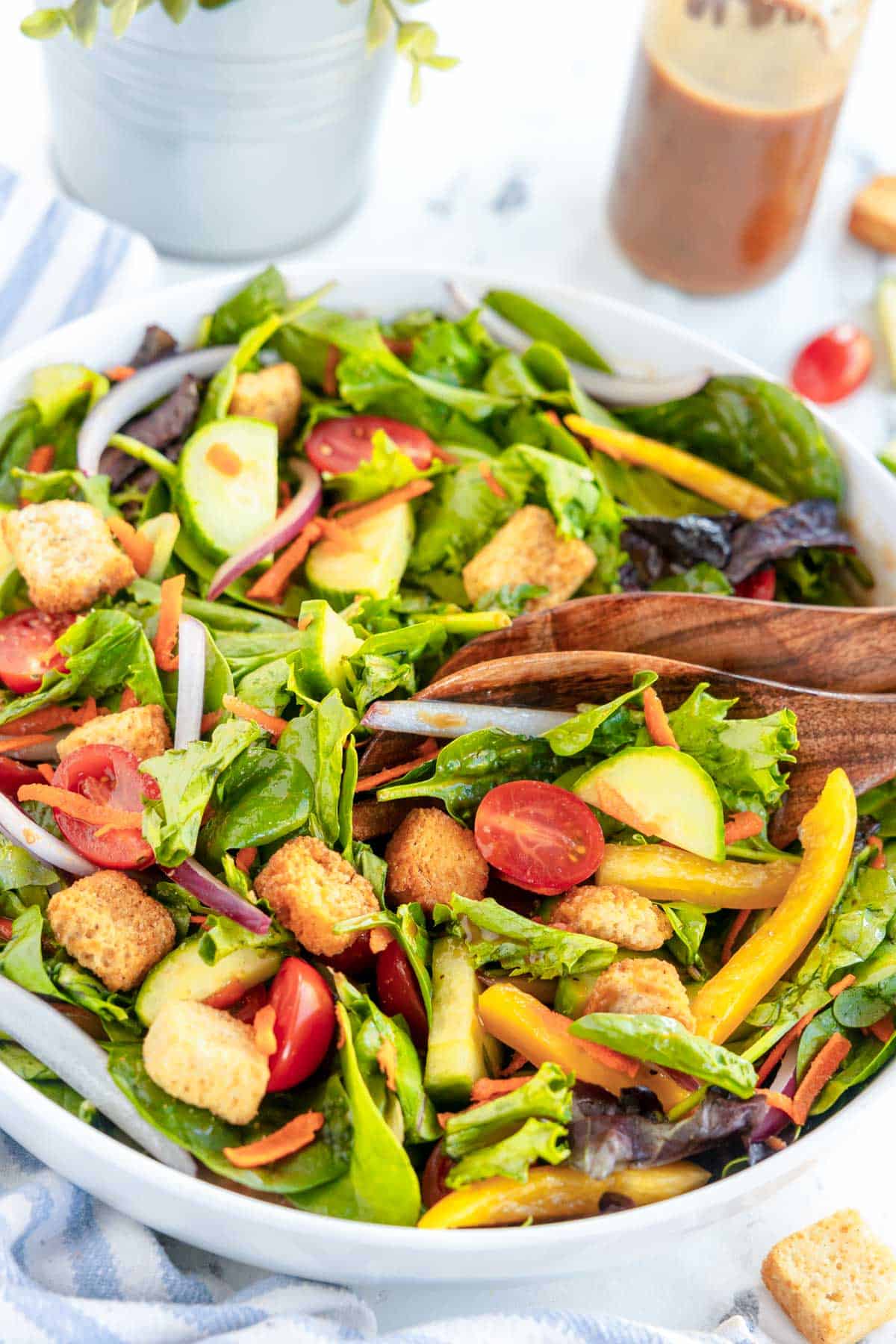 Garden salad with fresh vegetables and crunchy croutons, served in a clean white bowl with wooden salad servers.