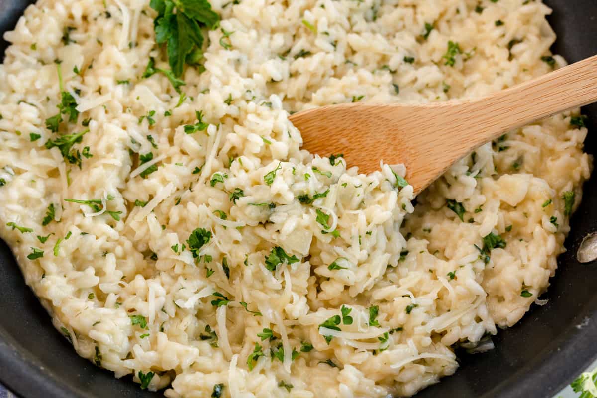 Creamy garlic parmesan risotto garnished with herbs in a black pan with a wooden spoon.