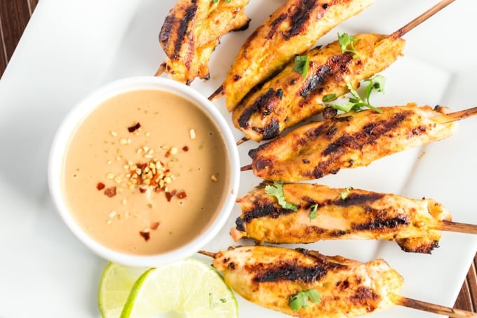 grilled chicken satay on a platter with peanut sauce and limes