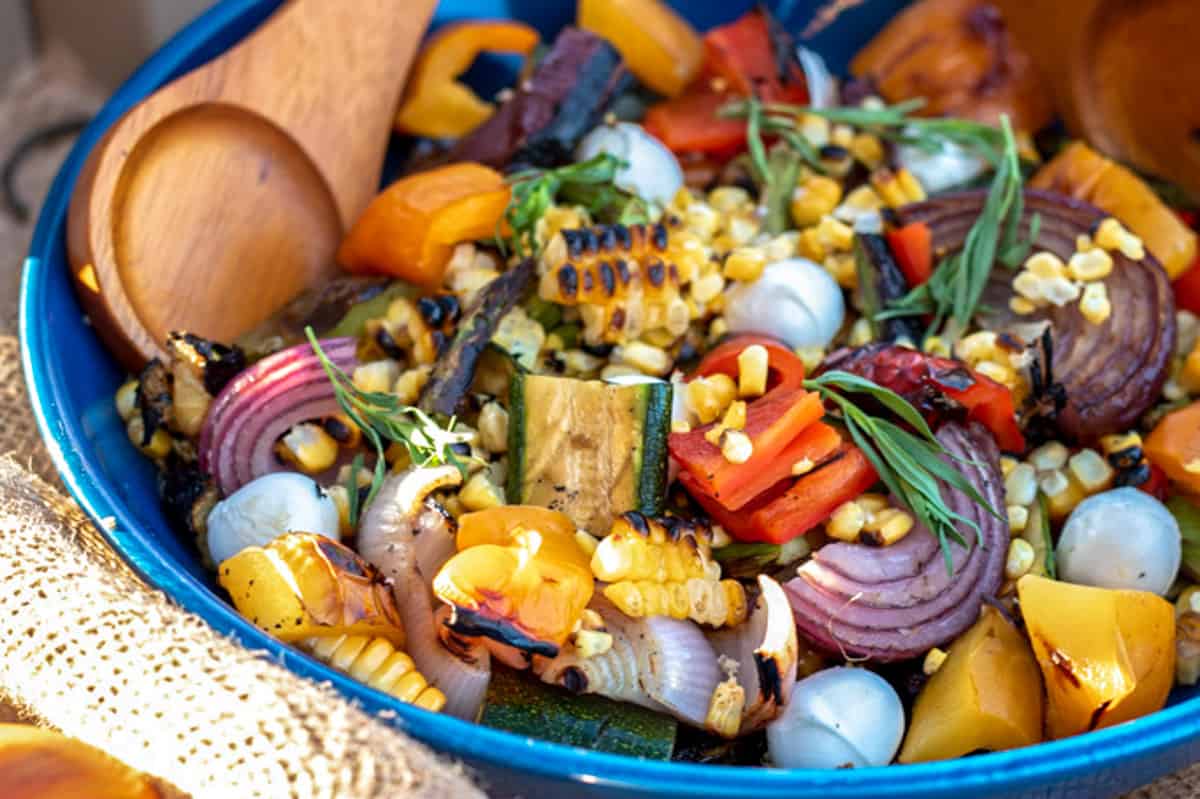 chopped grilled veggies in a blue bowl with wooden salad servers.