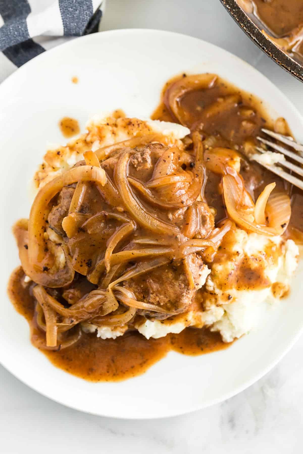 hamburger steak on a white plate smothered in onions