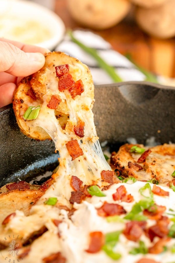 hand pulling irish nachos out of a cast iron skillet