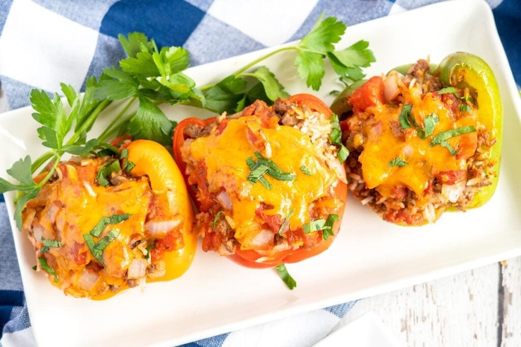 three stuffed peppers on a white platter with a blue and white napkin