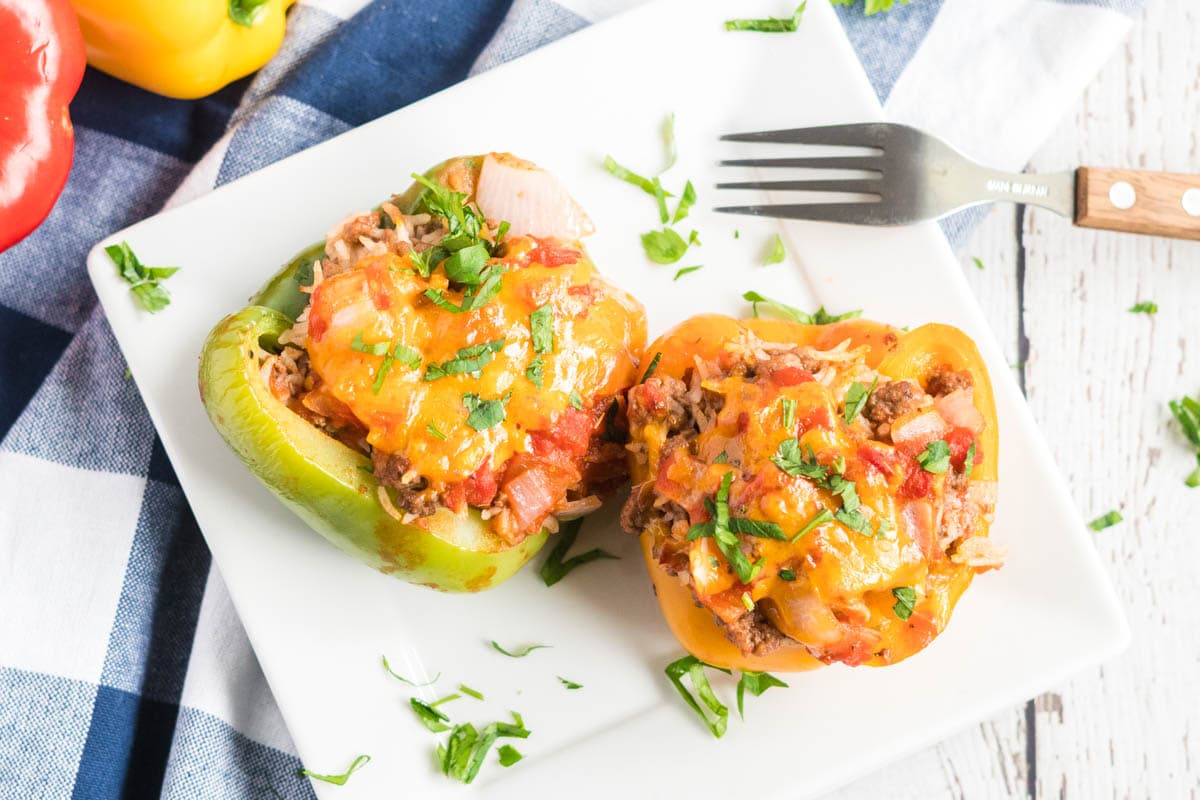 cooked stuffed peppers on a square white plate, with a blue and white napkin, and a fork