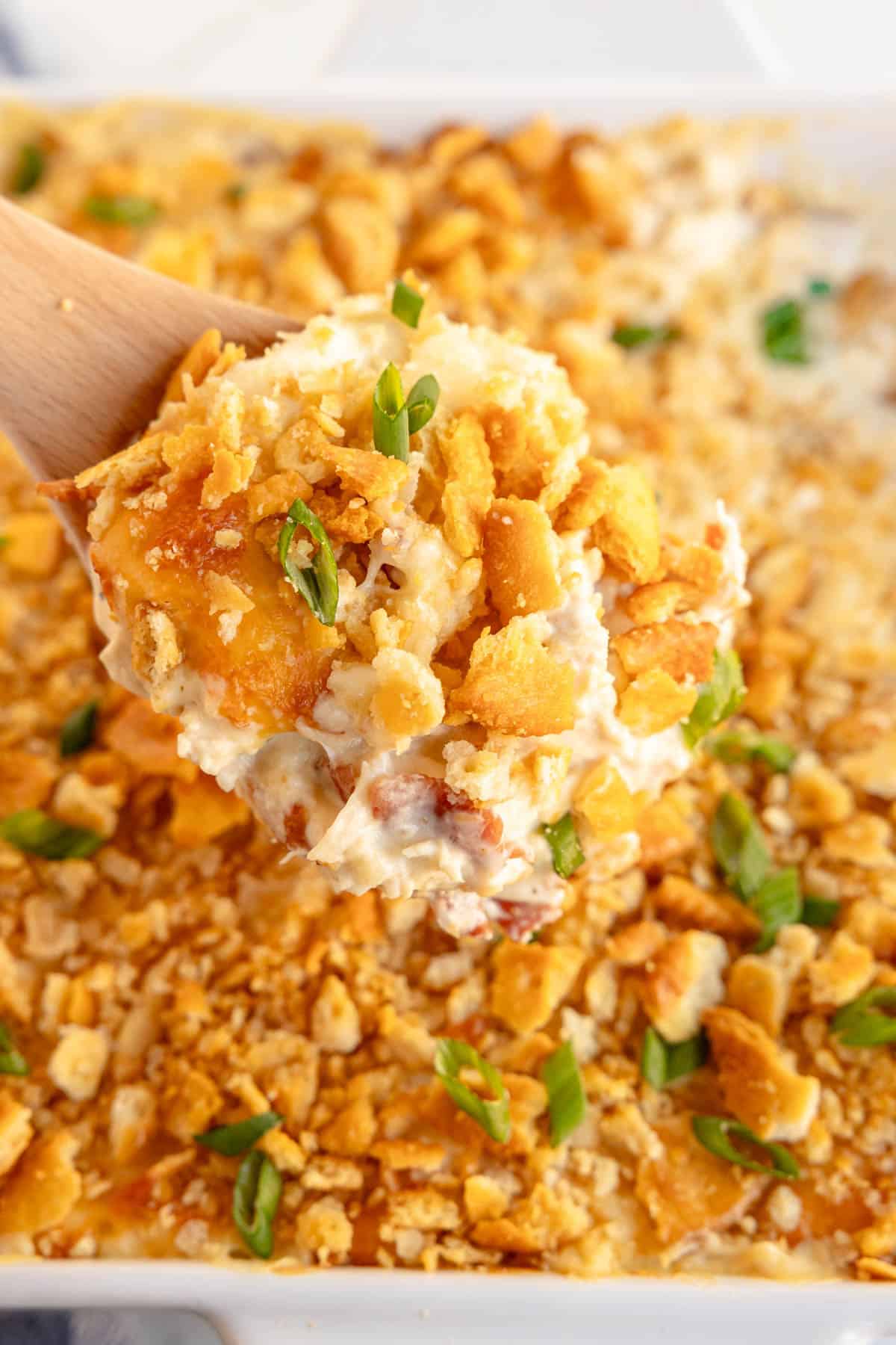 Taking a spoonful of Million Dollar Chicken Casserole out of a casserole dish.