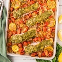 pesto salmon on a sheet pan with lemons and tomatoes.