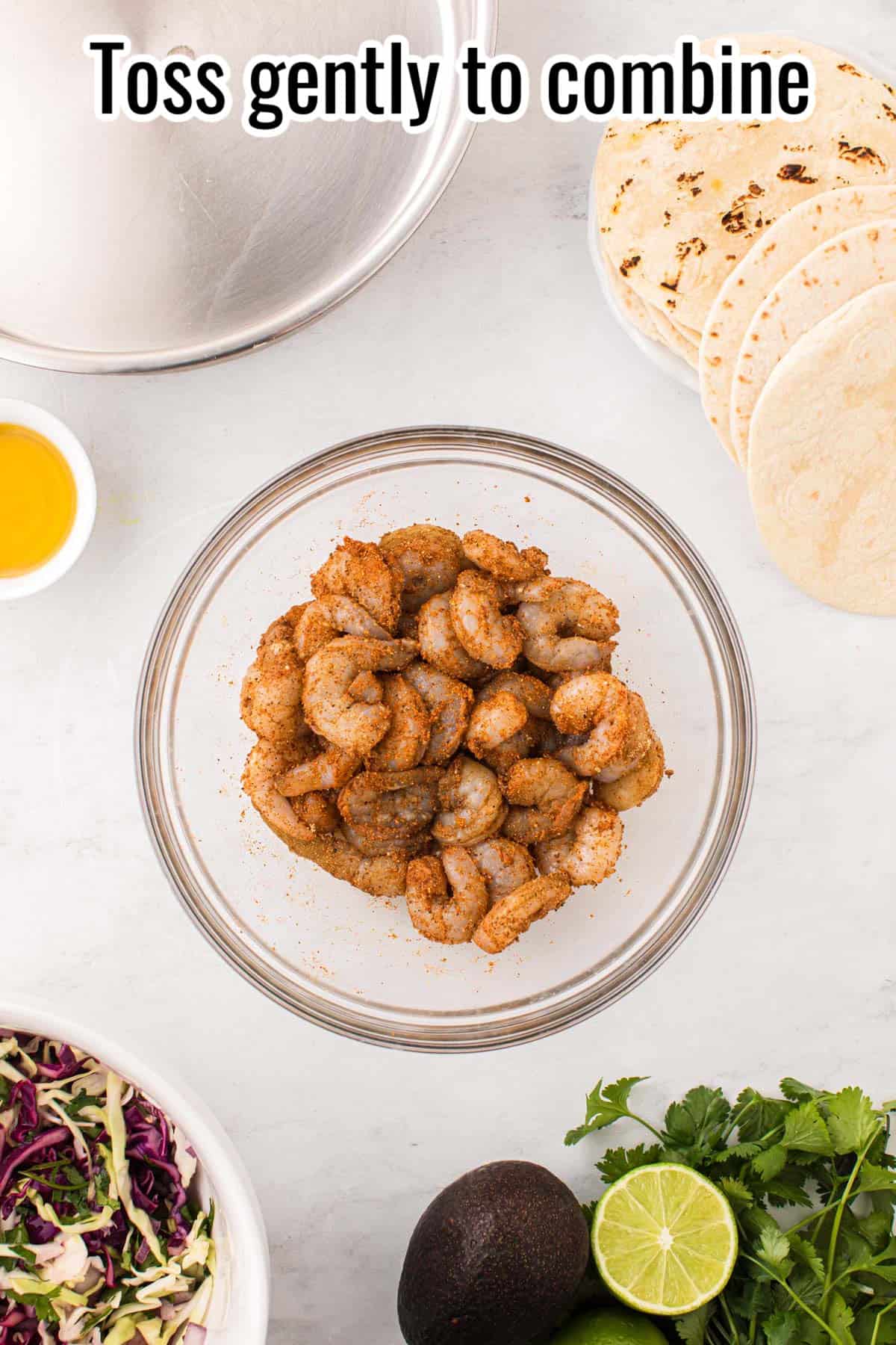 A clear bowl with raw shrimp and seasonings, mixed.