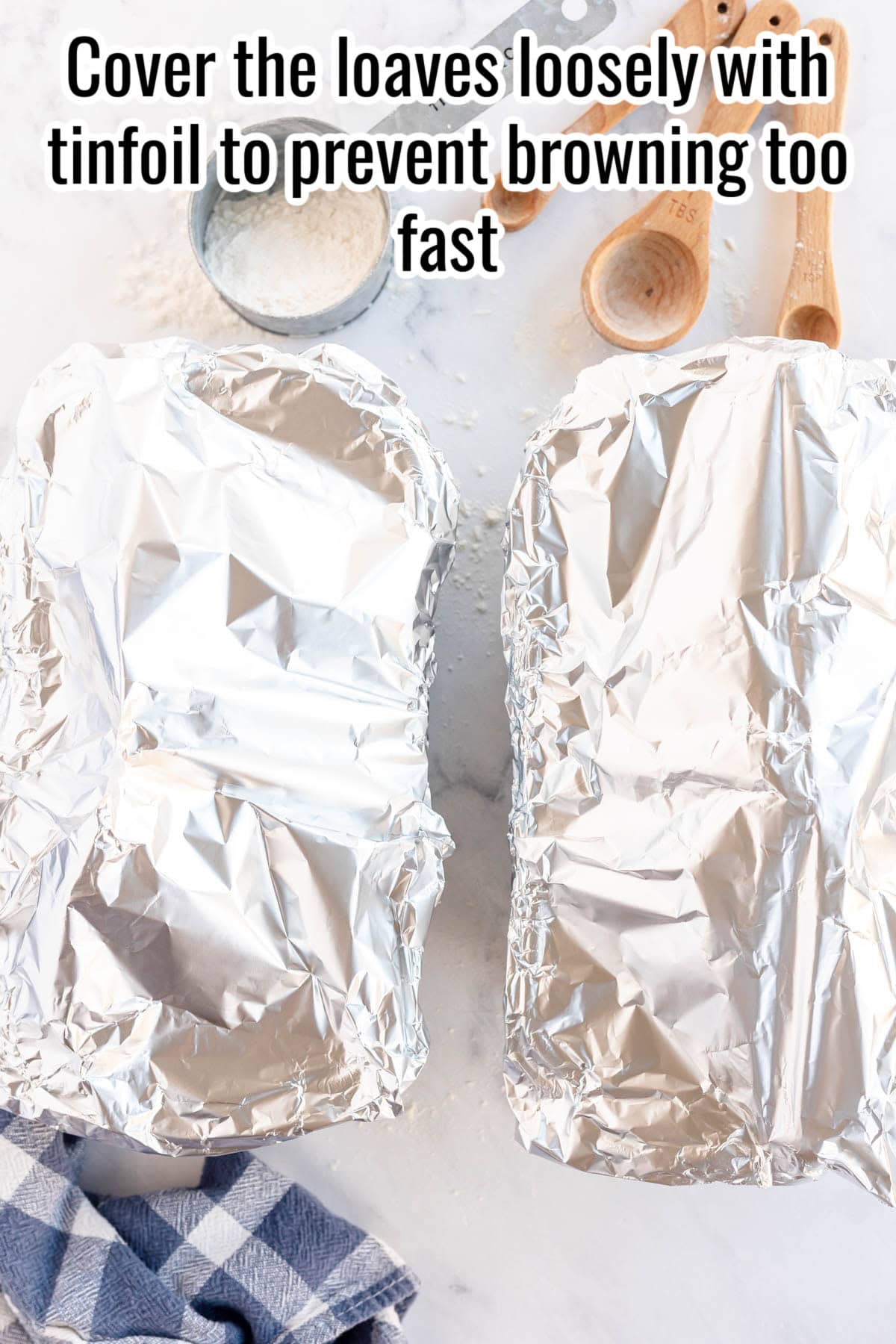 Two loaf pans covered with aluminum foil are on a white surface.