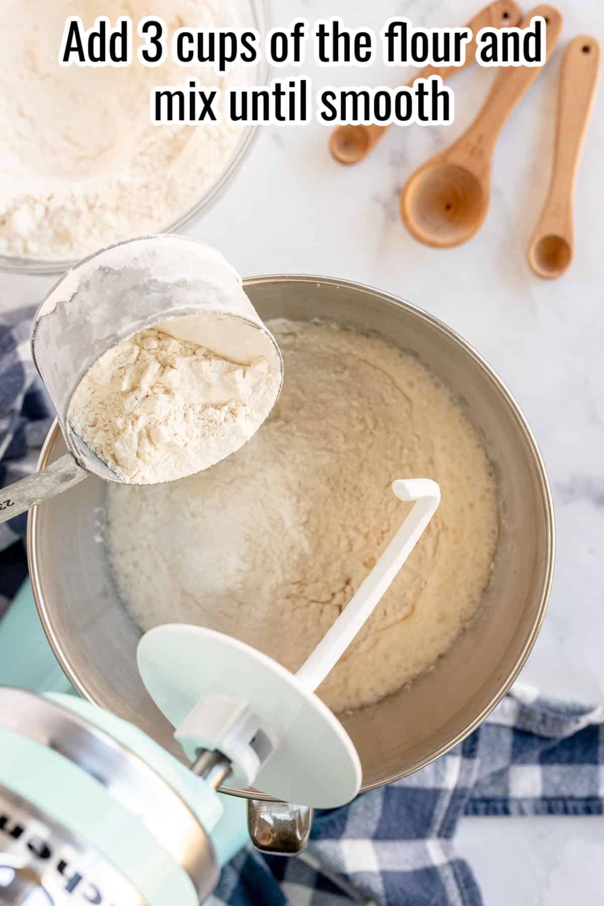 A mixing bowl with flour and a measuring cup pouring additional flour. The text above instructs to add 3 cups of flour and mix until smooth for perfect sandwich bread. Wooden measuring spoons are in the background.