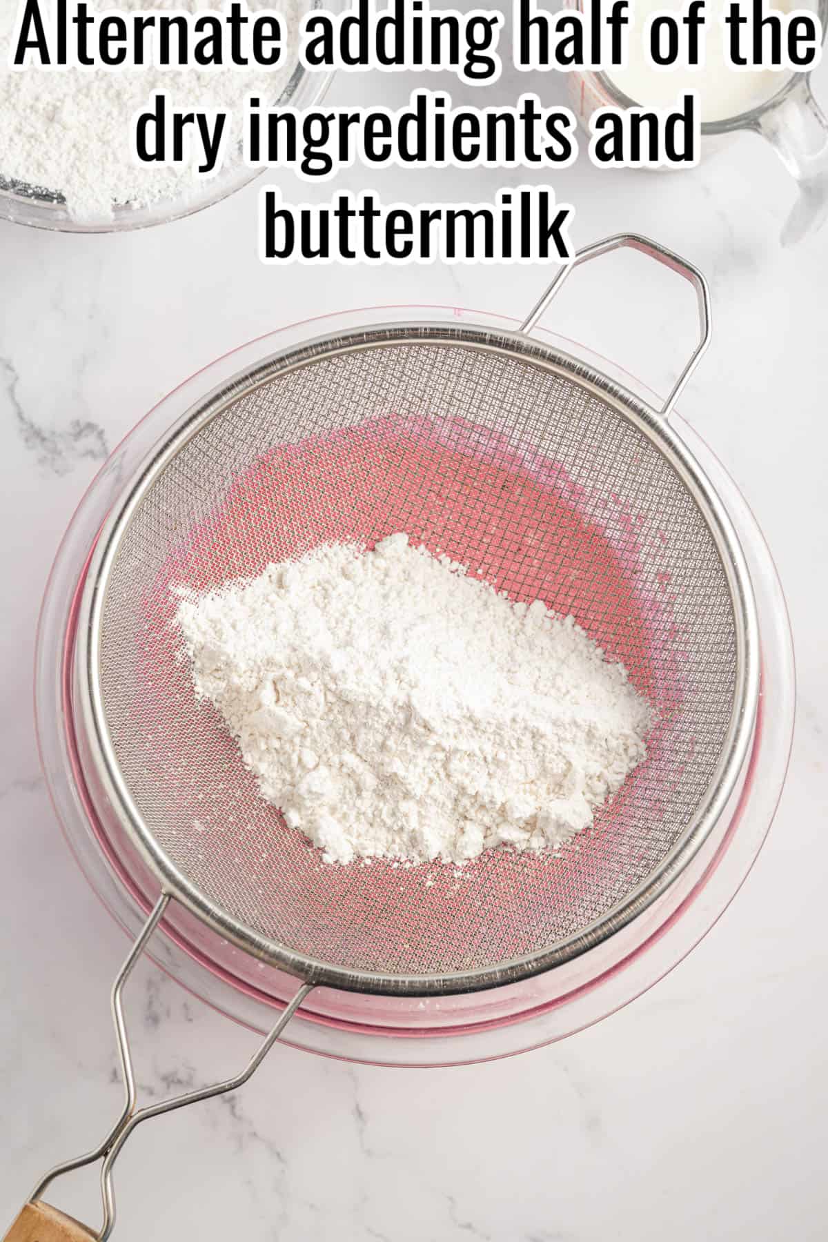 A sieve on top of a glass bowl with cake ingredients.