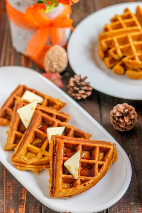 pumpkin waffles in quarters on a white plater with pinecones