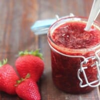 jar of strawberry jam with a spoon in it with strawberries alongside it