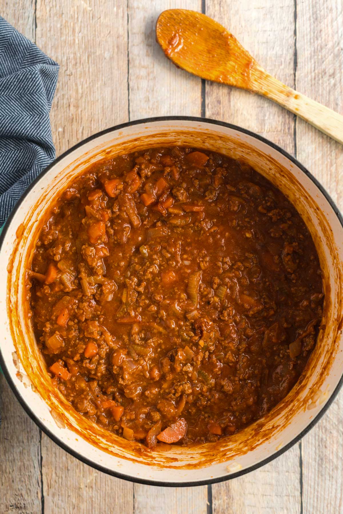 spaghetti bolognese in a dutch oven with a wooden spoon.