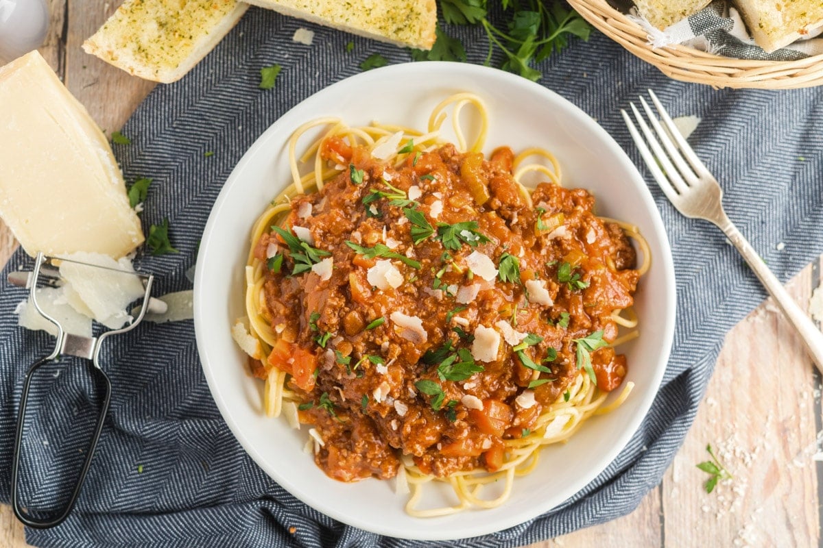 spaghetti bolognese in a white bowl with a fork and parmesan cheese