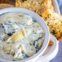 spinach artichoke dip in a white bowl with garlic bread toast