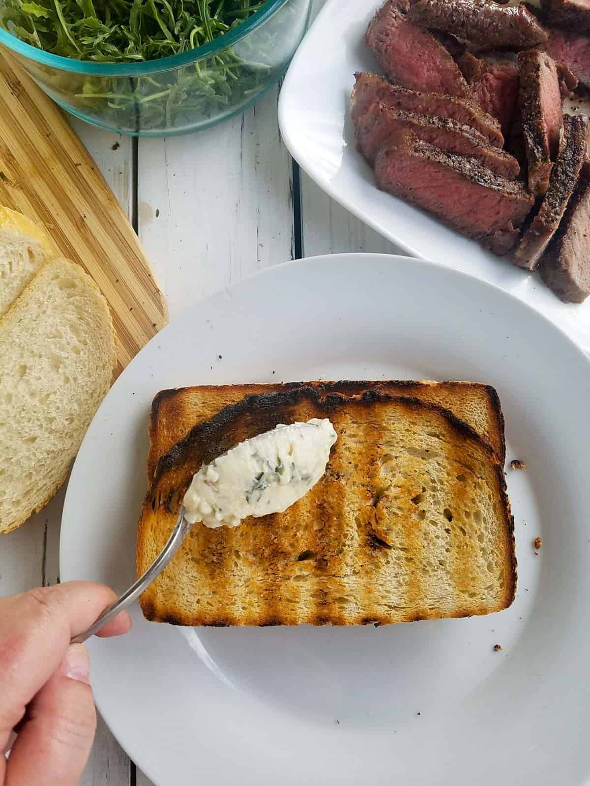 garlic butter being put on grilled bread with a spoon.