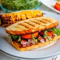 a steak sandwich with grilled bread on a white plate.