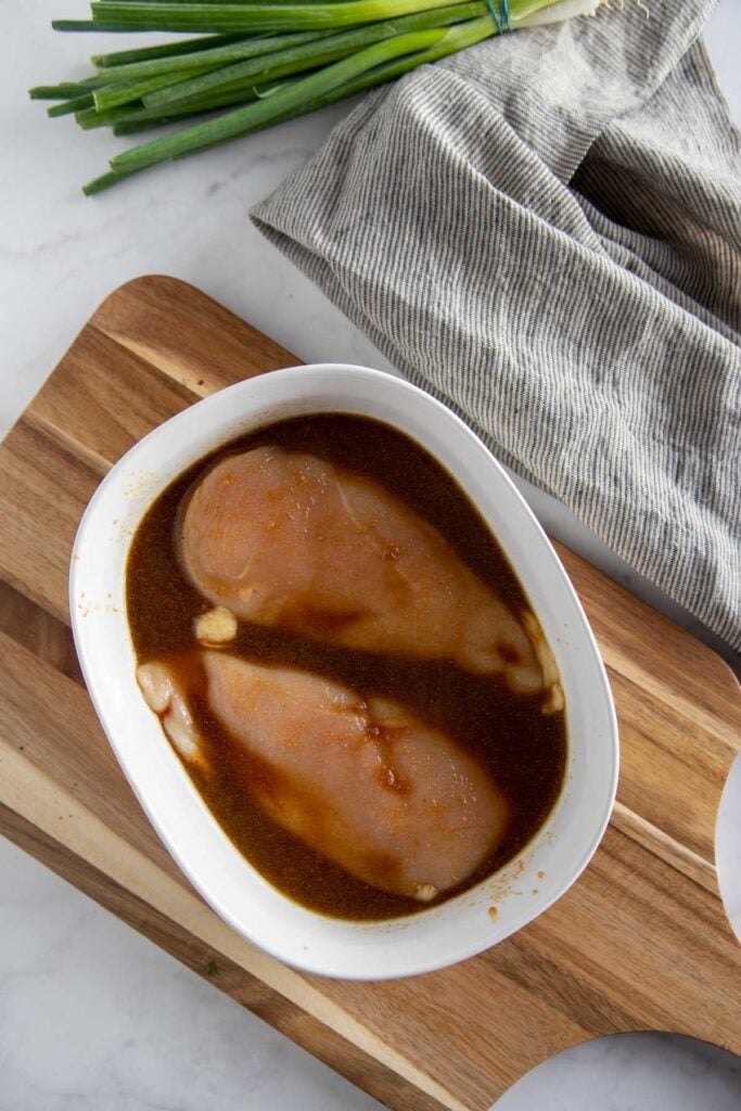 chicken being marinated in a white bowl.