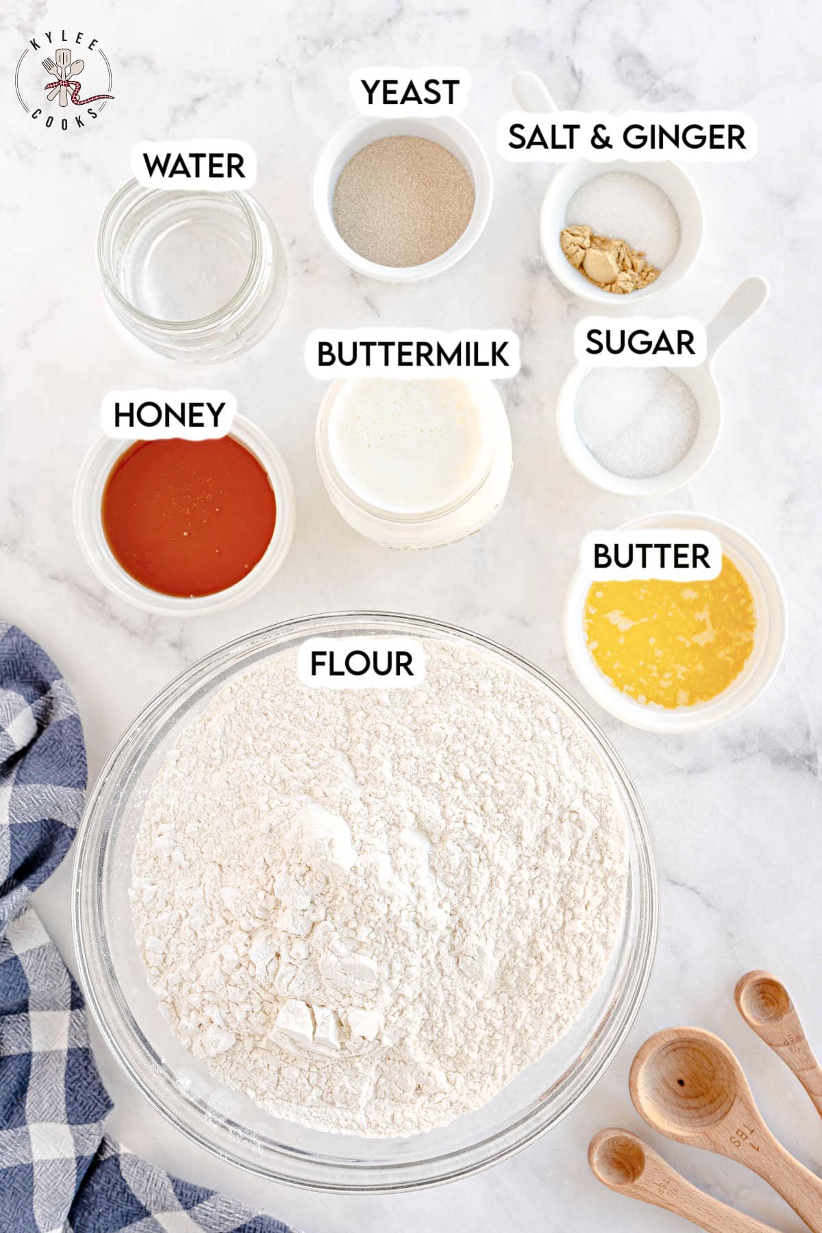 A collection of labeled ingredients, perfect for your next sandwich bread project, including flour, buttermilk, yeast, salt and ginger, sugar, butter, honey, and water placed in bowls and jars on a white surface.